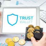 Trust Wallet is open on the tablet screen against the background of a wallet full of cryptocurrency coins.